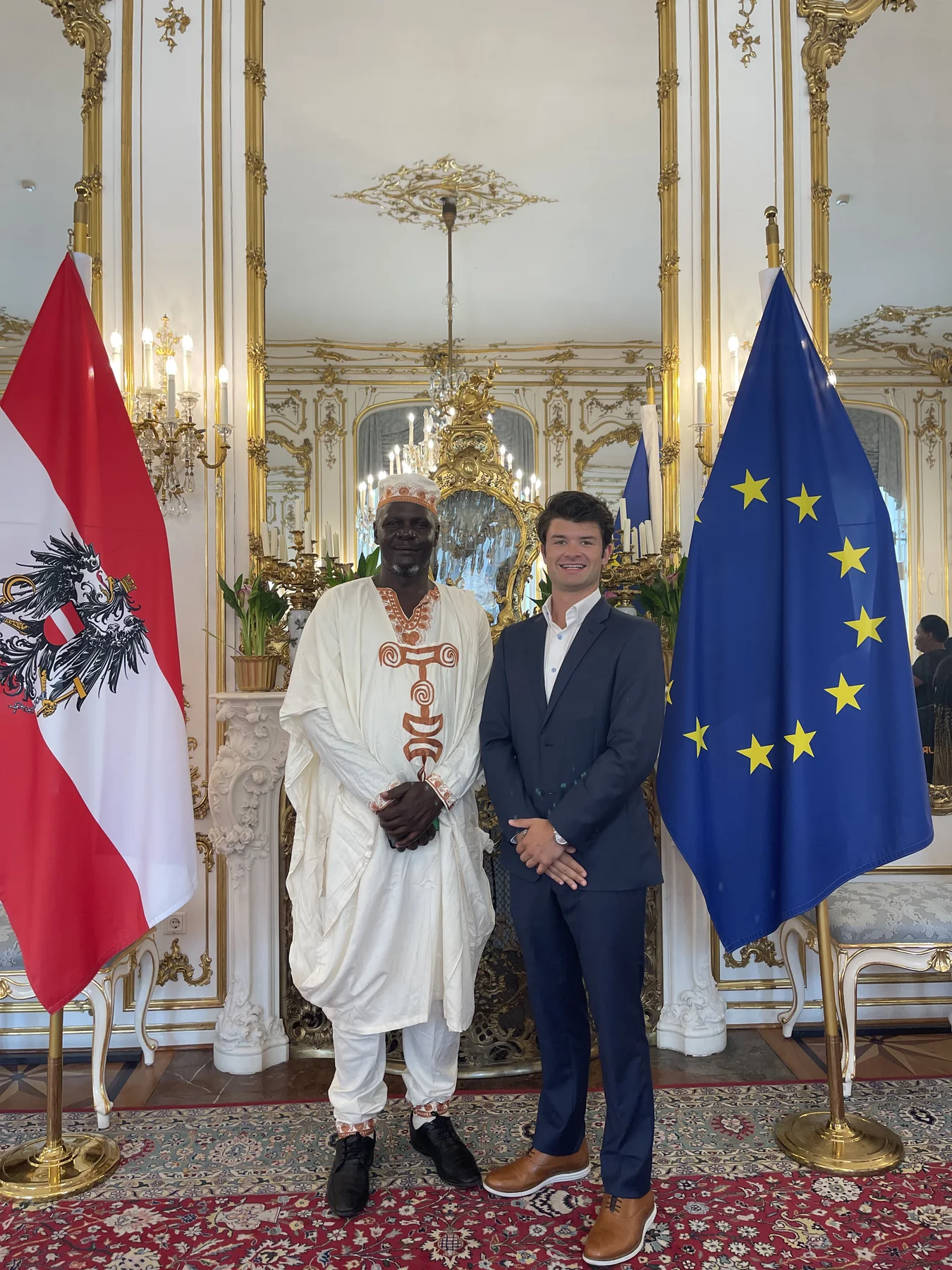 Raymond and Jack standing between the Austrian and European Union flags in an ornate reception room.