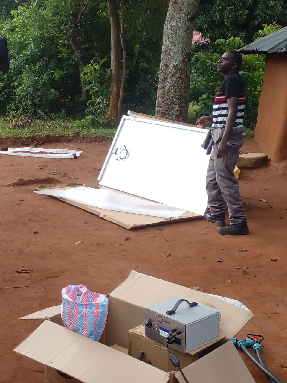 An adult installer standing beside solar panels and pump equipment at the project site.